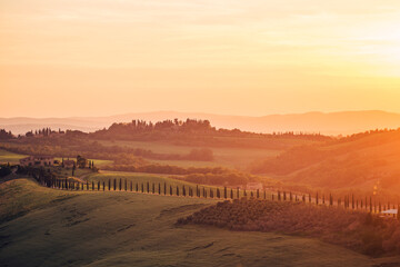 landscape of hills, country houses and trees in tuscany at sunset
