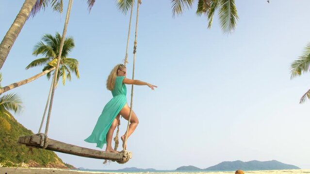 Woman spends her vacation at the seaside. The girl is swinging on a swing. Concept meditation, relaxation and walks, replenishment of energy and good happy mood.