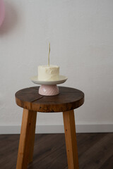 A small birthday cake, on a ceramic stand, wooden box, white background, beautiful decoration of a children's holiday
