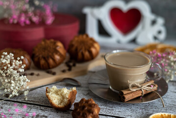 Composition of delicious festive breakfast homemade muffins and a cup of latte coffee on a wooden light background, flowers and a red box, close-up