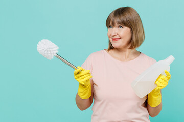 Elderly housewife woman 50s in t-shirt gloves hold toilet brush sponge detergent chemical bottle cleanser look aside isolated on plain pastel blue background. Housekeeping cleaning tidying up concept.