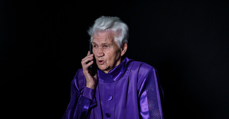 Elderly woman talking on a mobile phone on a black background
