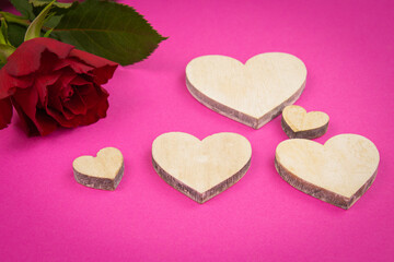 red rose on a pink background with wooden hearts