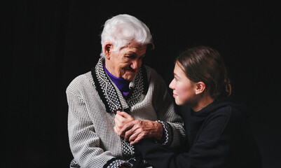 Elderly woman sitting with an adult granddaughter a black background.