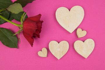 red rose on a pink background with wooden hearts