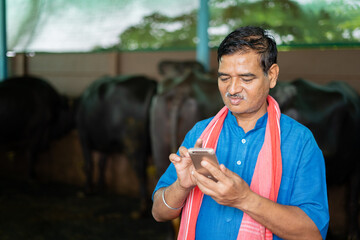 Indian milk dairy farmer busy using mobile phone at farm house - concept of technology, internet...