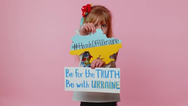 Toddler Ukrainian girl kid in embroidery dress protesting war conflict alone on pink background raises banner with inscription massage Be For The Truth Be With Ukraine. Peace, no war, stop aggression