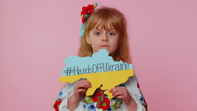 Portrait of Ukrainian girl child in embroidery dress showing banner with massage inscription text on map Hands Off Ukraine. Asking for help. Crisis, war, no peace, stop aggression from Russia country