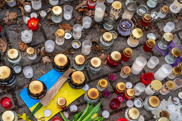 Candles, flowers and small Ukrainian flags on the pedestrian sidewalk in memory of those killed in...
