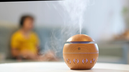 Modern aroma oil diffuser on the white table. Little boy in the background reading a book