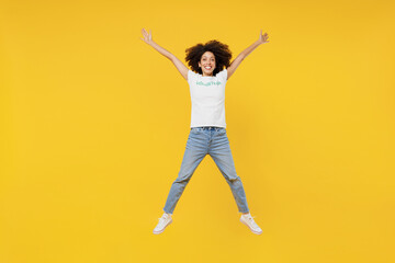 Fototapeta na wymiar Full body young woman of African American ethnicity in white volunteer t-shirt jump high with outstretched hands isolated on plain yellow background. Voluntary free work assistance help grace concept.