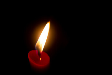 Red candle with yellow flame on black background