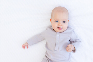 portrait of a newborn baby girl in a cotton suit on a white bed at home lying and smiling, a place...