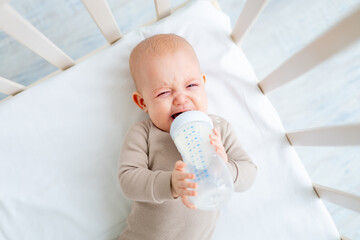 crying baby sucks a bottle of milk in a crib, baby food concept