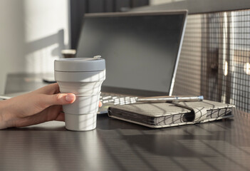 Woman holding takeaway cup and working on laptop. Businesswoman or student sitting at desk with planner and computer. Coffee break. High quality photo