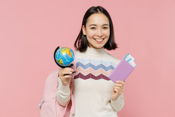 Traveler tourist student girl of Asian ethnicity wear sweater hold passport tickets globe isolated on plain pastel pink background. Passenger travel abroad weekends getaway Air flight journey concept