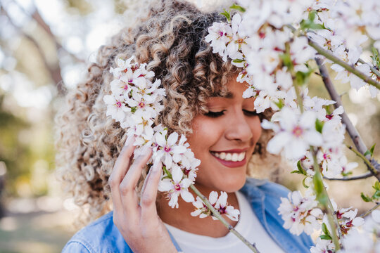 portrait of happy hispanic woman in spring among pink blossom flowers. selective focus on flowers