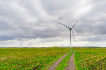 Large wind turbines with blades in the wind park on the background cloudy sky.