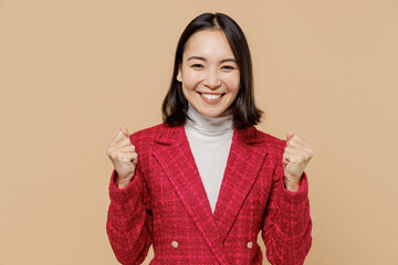 Smiling happy woman of Asian ethnicity in red jacket doing winner gesture celebrate clenching fists...