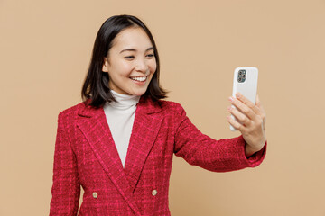 Smiling happy woman of Asian ethnicity 20s in red jacket doing selfie shot on mobile cell phone...