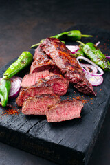 Traditional barbecue sirloin steak with chili and onion rings served as close-up on a charred wooden board