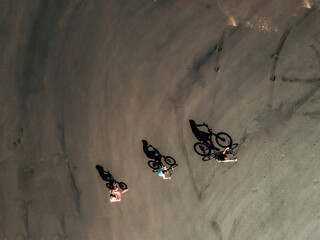 Three children on bikes ride across blacktop, photo taken from above so you can see their shadows