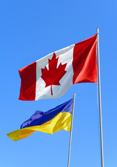 Flags of Ukraine and Canada are flying against the blue sky