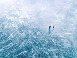 A father helps his son ice skate on a frozen lake, photographed from above
