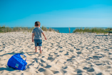 A toddler on a beach on Cape Cod stops playing with a bucket and walks down the sand to meet his father