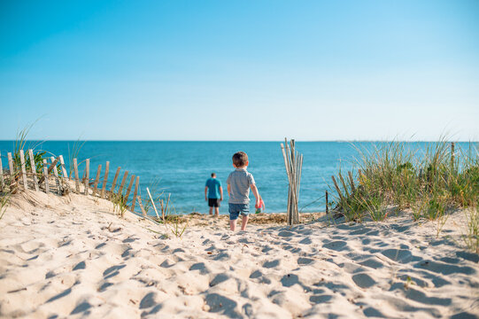 A toddler on a beach on Cape Cod stops playing with a bucket and walks down the sand to meet his father