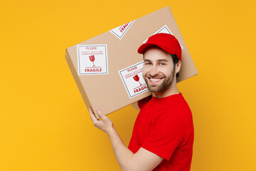 Side view happy delivery guy employee man in red cap T-shirt uniform workwear work as dealer...