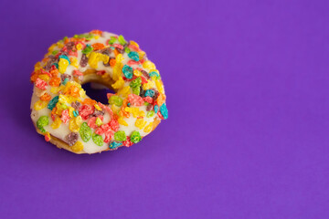 A fruity rice cereal topped iced donut by itself on a bright purple background