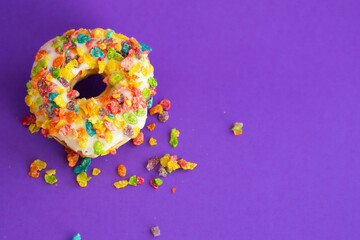 A fruity rice cereal topped iced donut by itself on a bright purple background