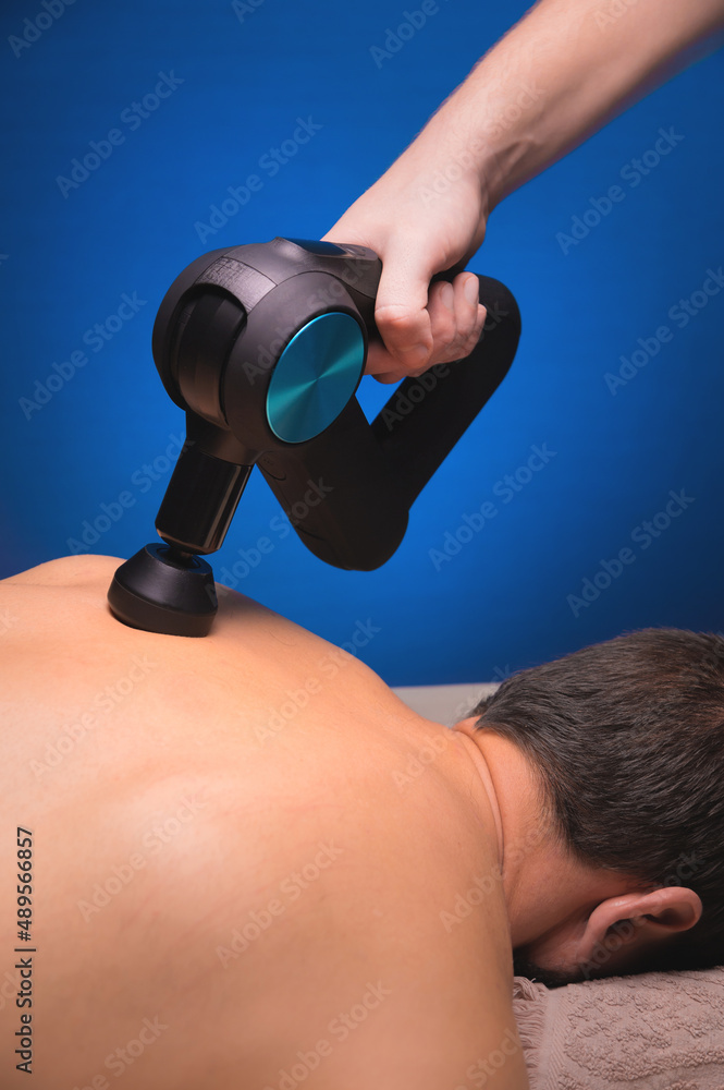 Canvas Prints Percussion massager in the hands of a masseur makes a massage of the shoulders and upper back to a male client lying down