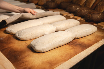 Women's hands carry out actions with raw bread. Dough before dipping into a bakery oven