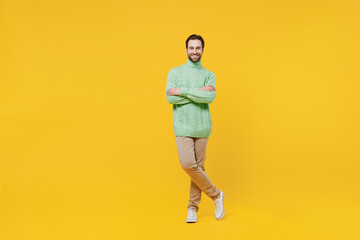 Full body smiling happy cheerful young man 20s wearing mint knitted sweater hold hands crossed folded look camera isolated on plain yellow background studio portrait. People lifestyle fashion concept.