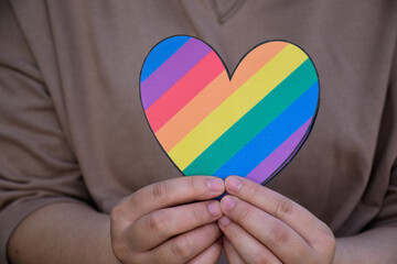 Two hearts made of rainbow colored paper are holding in hands of the LGBT person, concept for lgbtq+ communities celebrations in pride month around the world.