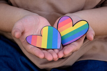Two hearts made of rainbow colored paper are holding in hands of the LGBT person, concept for lgbtq+ communities celebrations in pride month around the world.