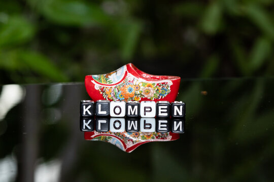 Mote alphabet blocks arranged into "Klompen" with klompen footwear background.