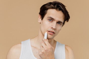 Attractive sexy young man 20s perfect skin in undershirt hold lipstick use apply lip balm isolated...