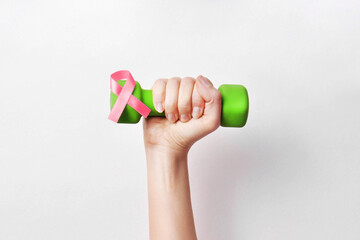A dumbbell with a pink ribbon in the hands of a woman. A symbol of victory over breast cancer
