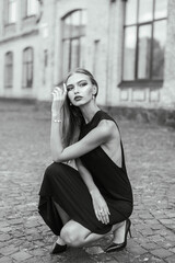 Black and white photo Portrait of a girl with long straight hair in a black dress on the background of an ancient stone building