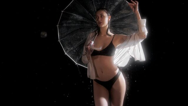 Hot young woman with sexy body posing under the rain holding an umbrella