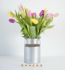 pink, yellow and purple tulips in silver metal milk can with wooden letters