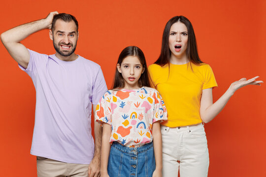 Young confused sad happy parents mom dad with child kid daughter teen girl in basic t-shirts scratch head spread hands isolated on yellow background studio. Family day parenthood childhood concept