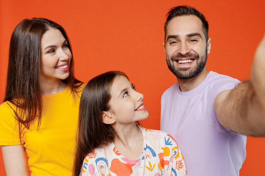 Close up young fun happy parents mom dad with child kid daughter teen girl in basic t-shirts do selfie shot pov on mobile phone isolated on yellow background. Family day parenthood childhood concept