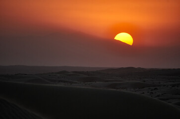 yellow sunset over the desert sun behind orange clouds sand in foreground 