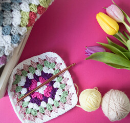 colorful granny square pattern with crochet hook and woolen balls  on pink ground 