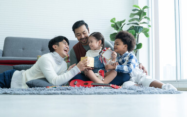 Asian young LGBTQ gay family giving gift to little kids Caucasian adopted daughter and African son...