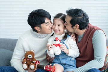Asian young LGBTQ gay couple kissing cheek of little Caucasian adopted kid together at home. Happy...